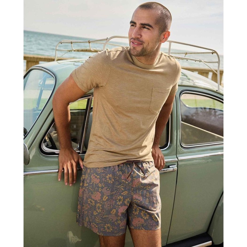 A man in a khaki Toad & Co Men's Tempo Short Sleeve Pocket Crew leans against a vintage car by the ocean.