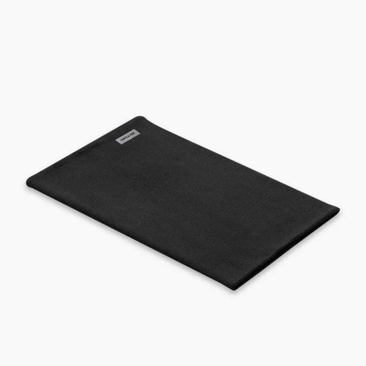 A flat lay photo of the Turtle Fur Carefree Merino Wool Pipe Dream in Black, showing the rectangular shape and a small label on the top left corner against a white background.