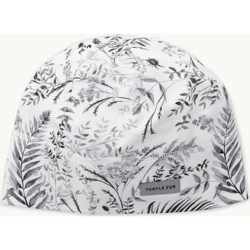 A top-down view of the Turtle Fur Women's Comfort Shell Brain Shroud in PowderDayFronds with a botanical print and a small tag.