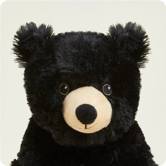 A close-up front view of the Warmies Bear with its black fur and cream-colored snout against a plain light background.