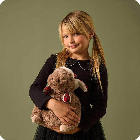 A girl in a black dress holds the Warmies Cozy Capybara against a green background.