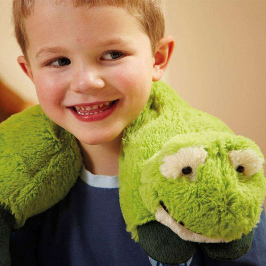 A young boy smiles wearing the Warmies Frog Cozy Wraps, a green plush frog-shaped neck warmer with a smiling face.