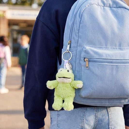 Back view of the Warmies Frog Keyring attached to a light blue backpack with a green stuffed frog toy hanging from it.