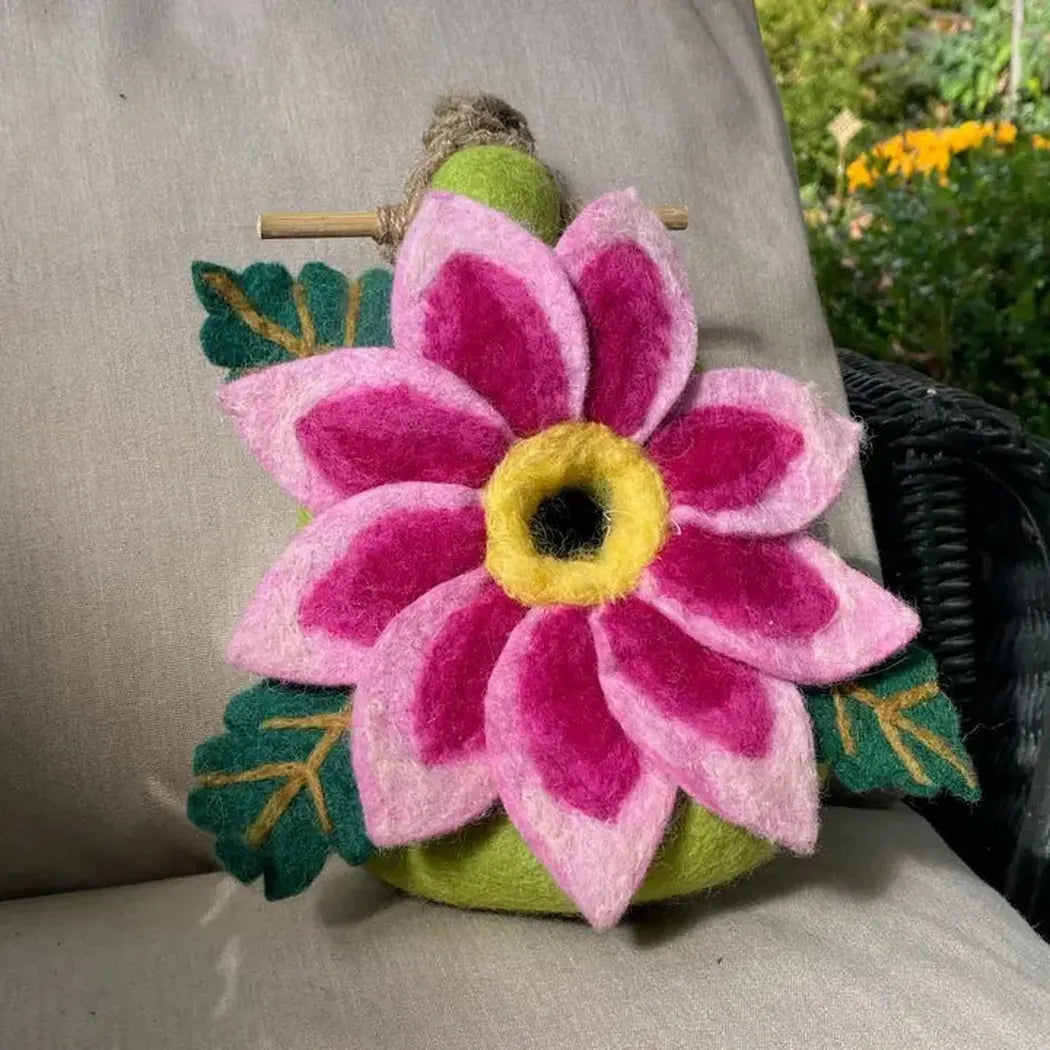 A close-up of the Wild Woolies Dahlia Star Birdhouse on a light-colored chair with green leaves and a garden background.