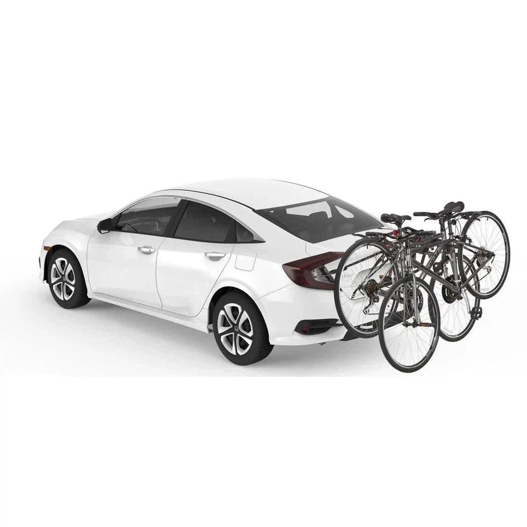 A white sedan with a Yakima HangOut car rack holding two bicycles is shown from a rear three-quarter angle against a plain white background.