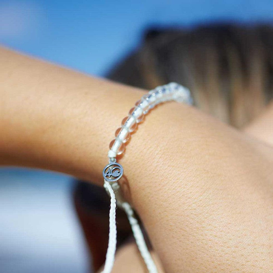 A close-up of a person’s arm wearing the 4Ocean Deep Sea Beaded Bracelet in Saltwater Glow, with a blue sky background.