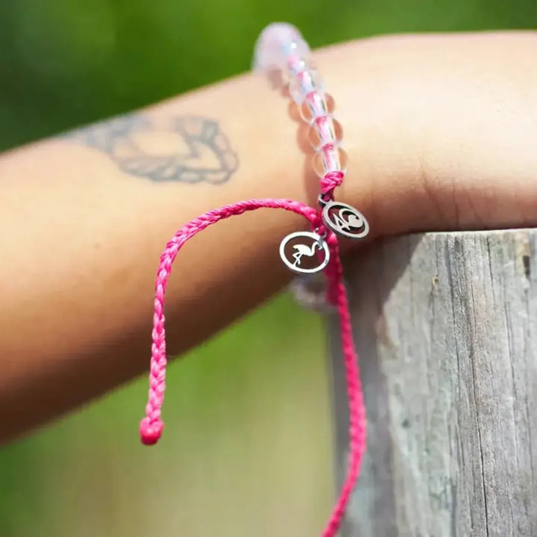 A pink 4Ocean Flamingo bracelet with charms rests on a wooden post outdoors.