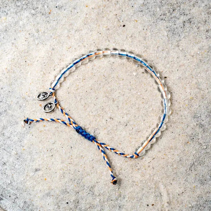 A close-up of the 4Ocean Reef Shark Beaded Bracelet - July 2024 Limited Edition on a light gray textured surface, showing the beaded design and blue and orange cord.