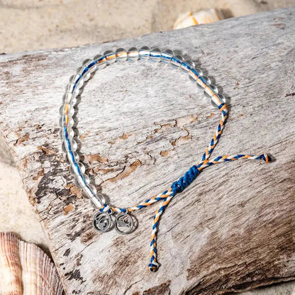 A close-up of the 4Ocean Reef Shark Beaded Bracelet - July 2024 Limited Edition on a piece of driftwood with a shell nearby.