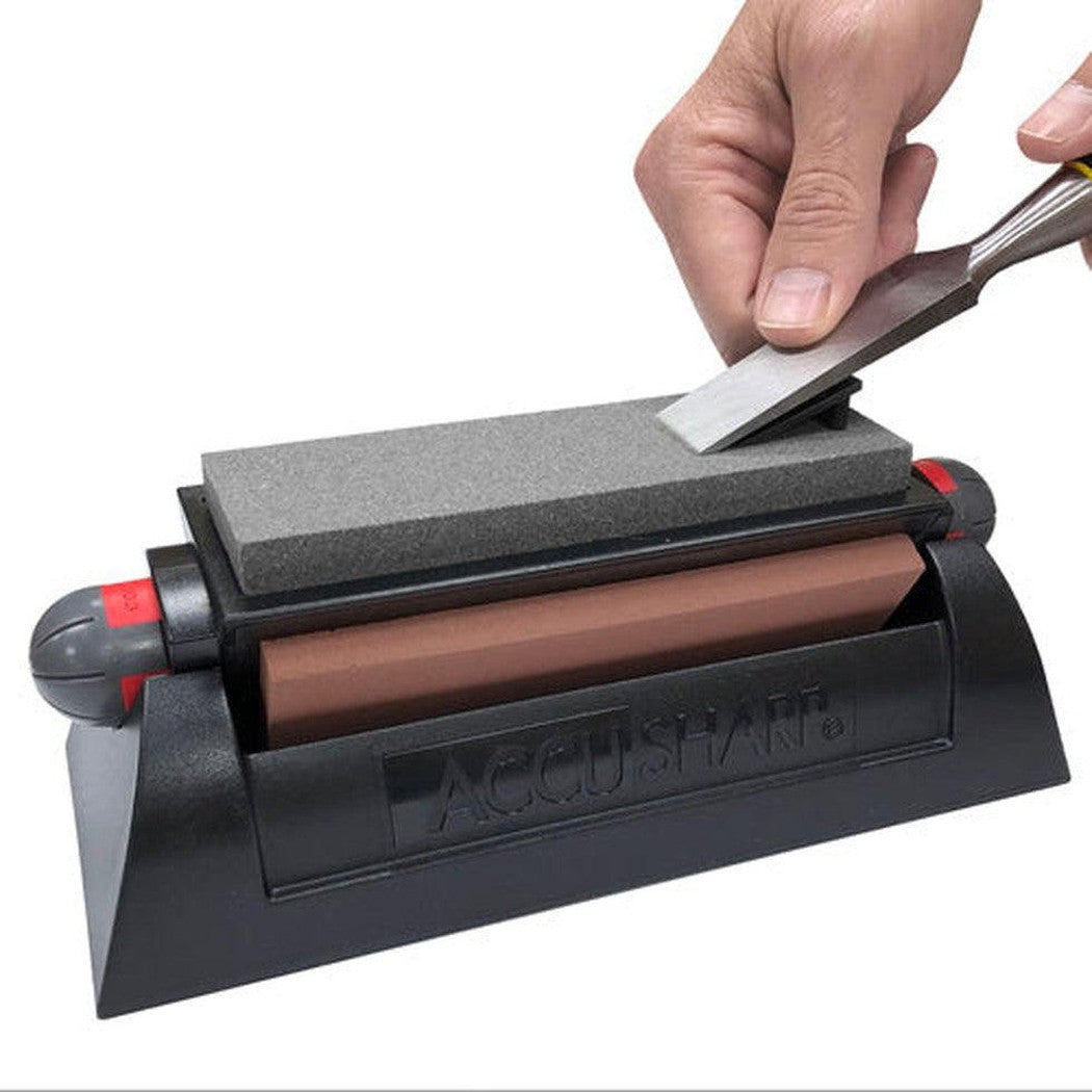 A hand uses the AccuSharp Tri-Stone System on a knife, showing the charcoal stone and brown base against a white background.
