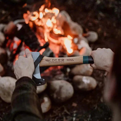 A person holds the Adler Hatchet with a green and black handle in front of a campfire.