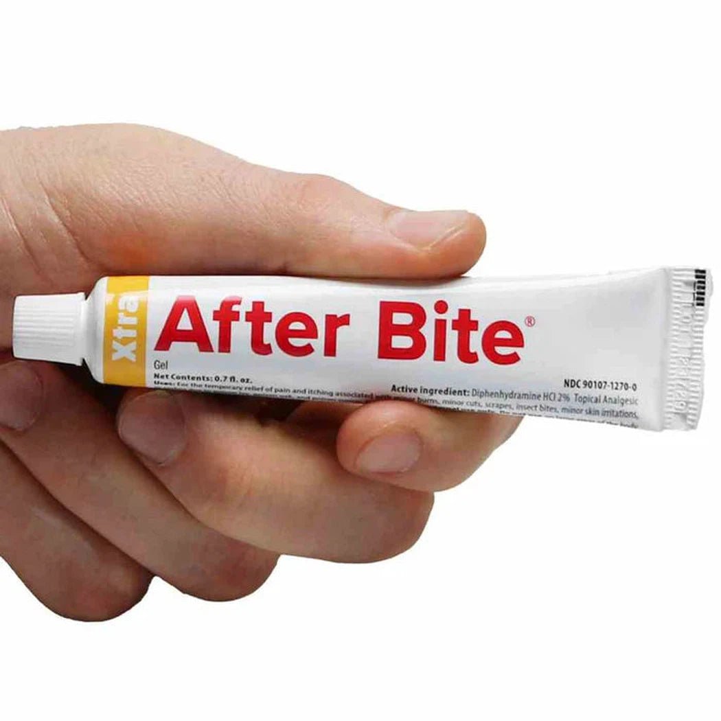Hand holding a white tube of Adventure Medical Kits After Bite Xtra with red text against a white background.