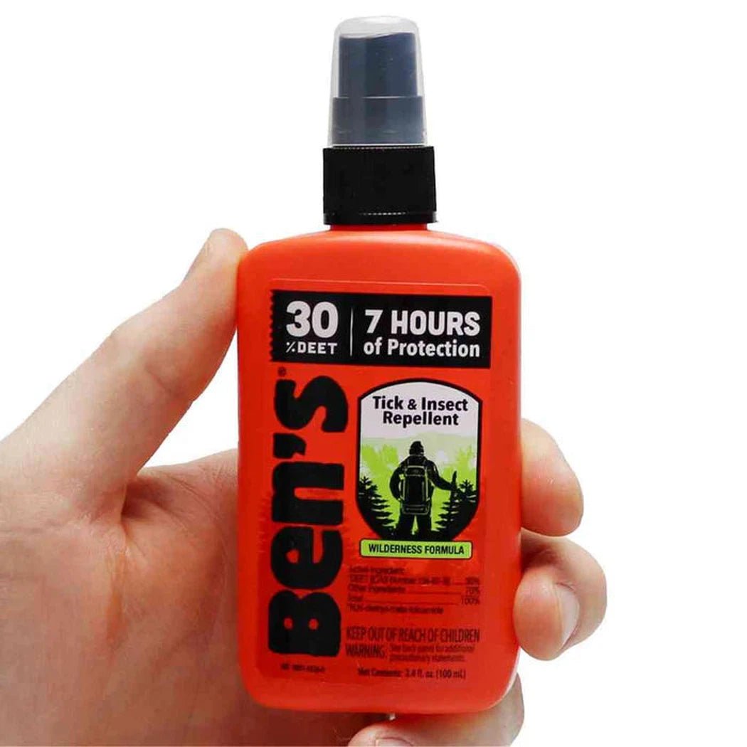A hand holds an orange Ben's 30 Tick & Insect Repellent pump spray bottle with a black cap and clear nozzle against a white background.