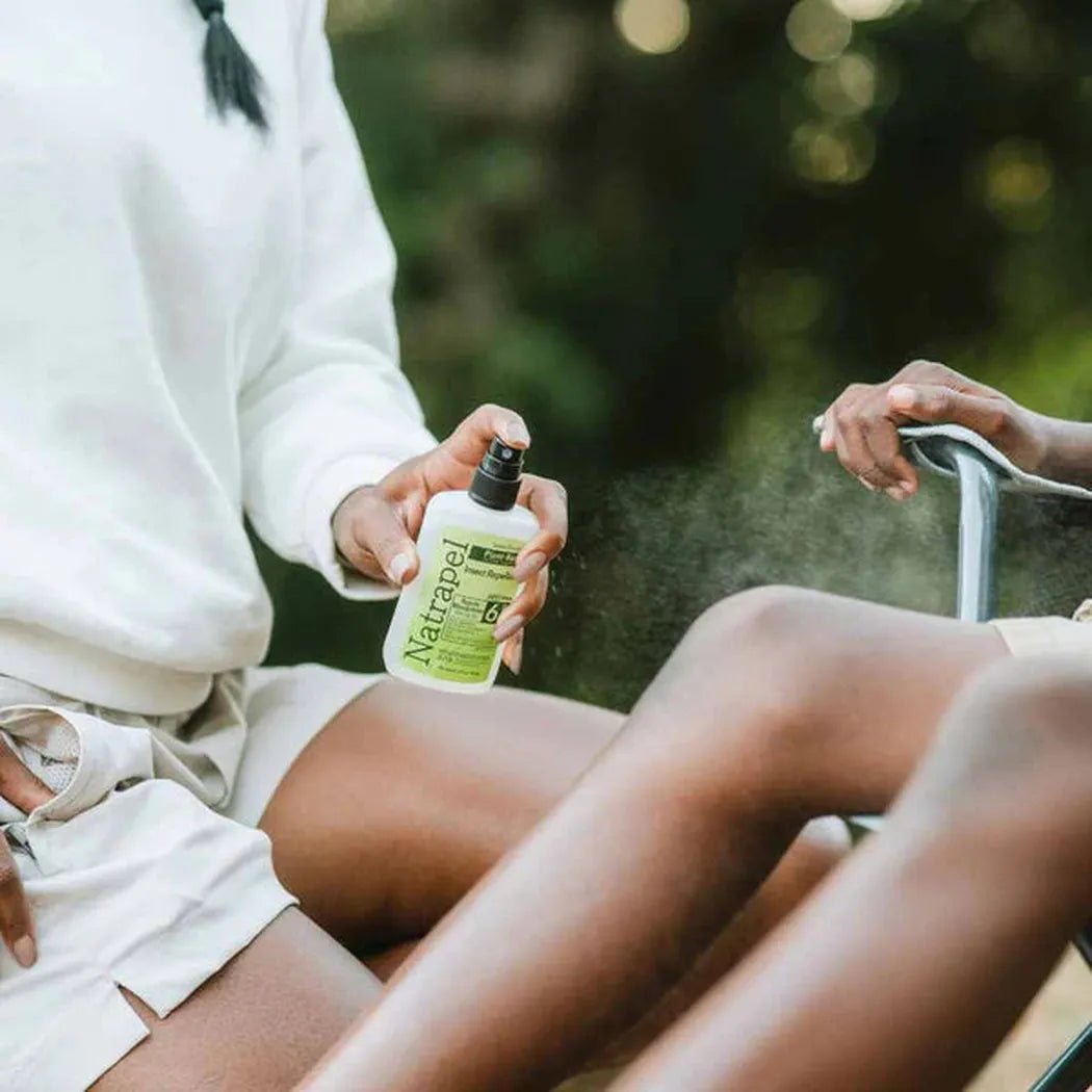 A person sprays Natrapel Lemon Eucalyptus Pump 3.4oz on their leg while sitting outdoors.