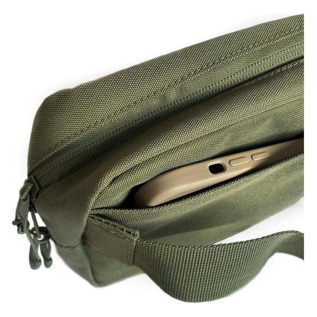 A close-up of the Adventurist Backpack Co. Summit Sling Bag in Black showing the front zip pocket with a phone inside against a white background.