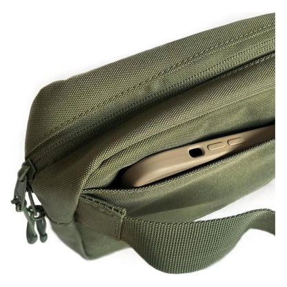 A close-up of the Adventurist Backpack Co. Summit Sling Bag in Black showing the front zip pocket with a phone inside against a white background.