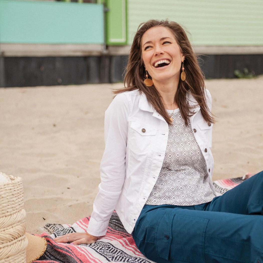 A woman sits on a blanket outdoors wearing the White Aventura Women's Arden V2 Jacket.