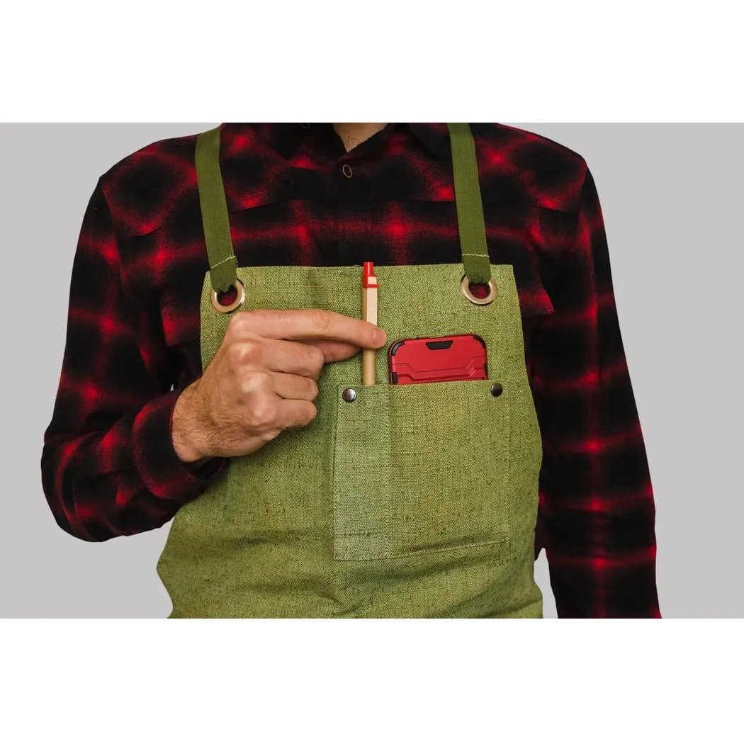 A person in a red and black plaid shirt wears the Beavercraft Adjustable Green Canvas Work Apron with a red phone and pencil in the pocket, against a gray background.