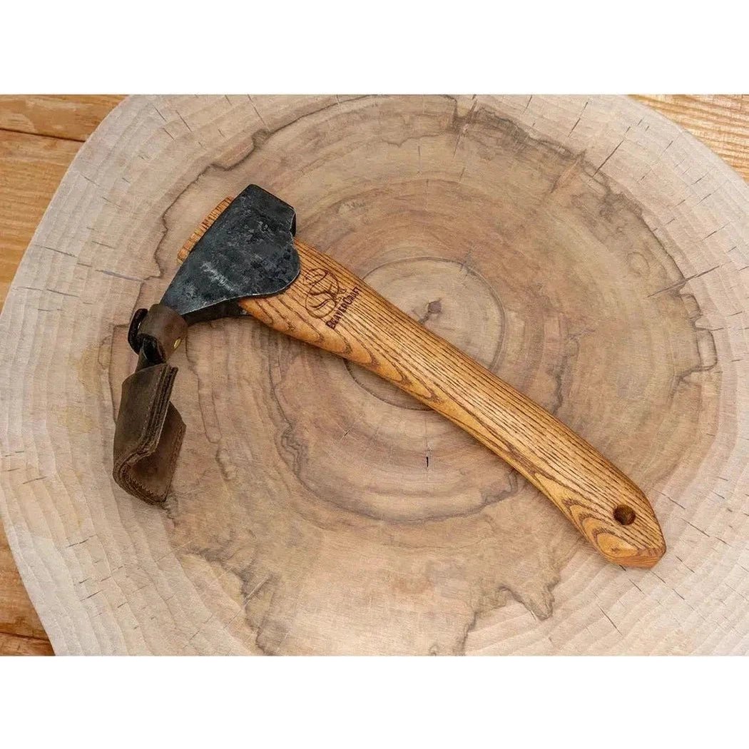 A Beavercraft Adze with Leather Sheath rests on a large, round wooden slice with visible tree rings.
