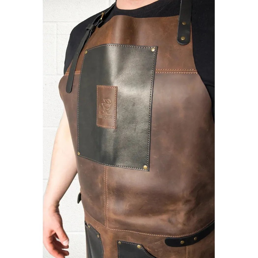 A front view of the Beavercraft Cowhide Apron Leather with a black patch and brass rivets on a white brick background.