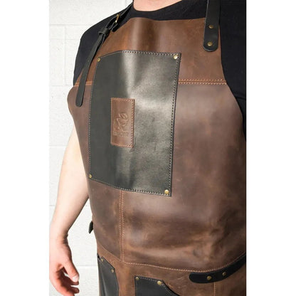 A front view of the Beavercraft Cowhide Apron Leather with a black patch and brass rivets on a white brick background.