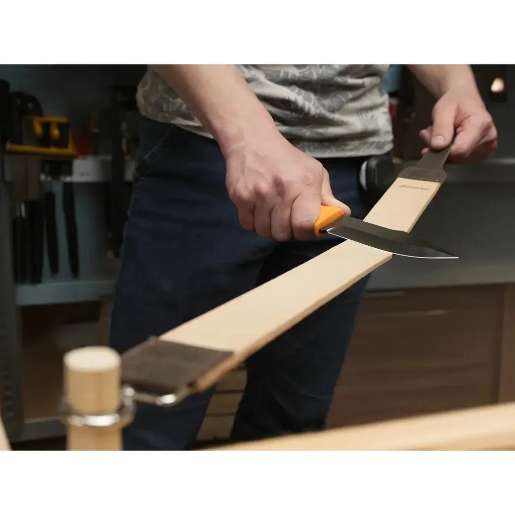 A person uses the Beavercraft Double-Sided Leather Hanging Strop on a wooden board in a workshop setting.