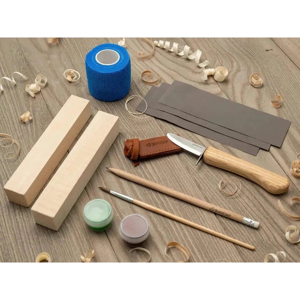A top-down view of the Beavercraft Kids Carving Hobby Kit on a wooden surface with wood shavings.
