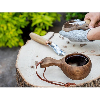 A top-down view of the Beavercraft Kuksa Carving Kit on a tree stump with green foliage in the background.