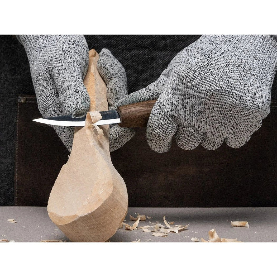 A person carves wood with the Beavercraft Luxury Spoon Carving Set With Walnut Handles, showing the knife and wood shavings on a work surface.