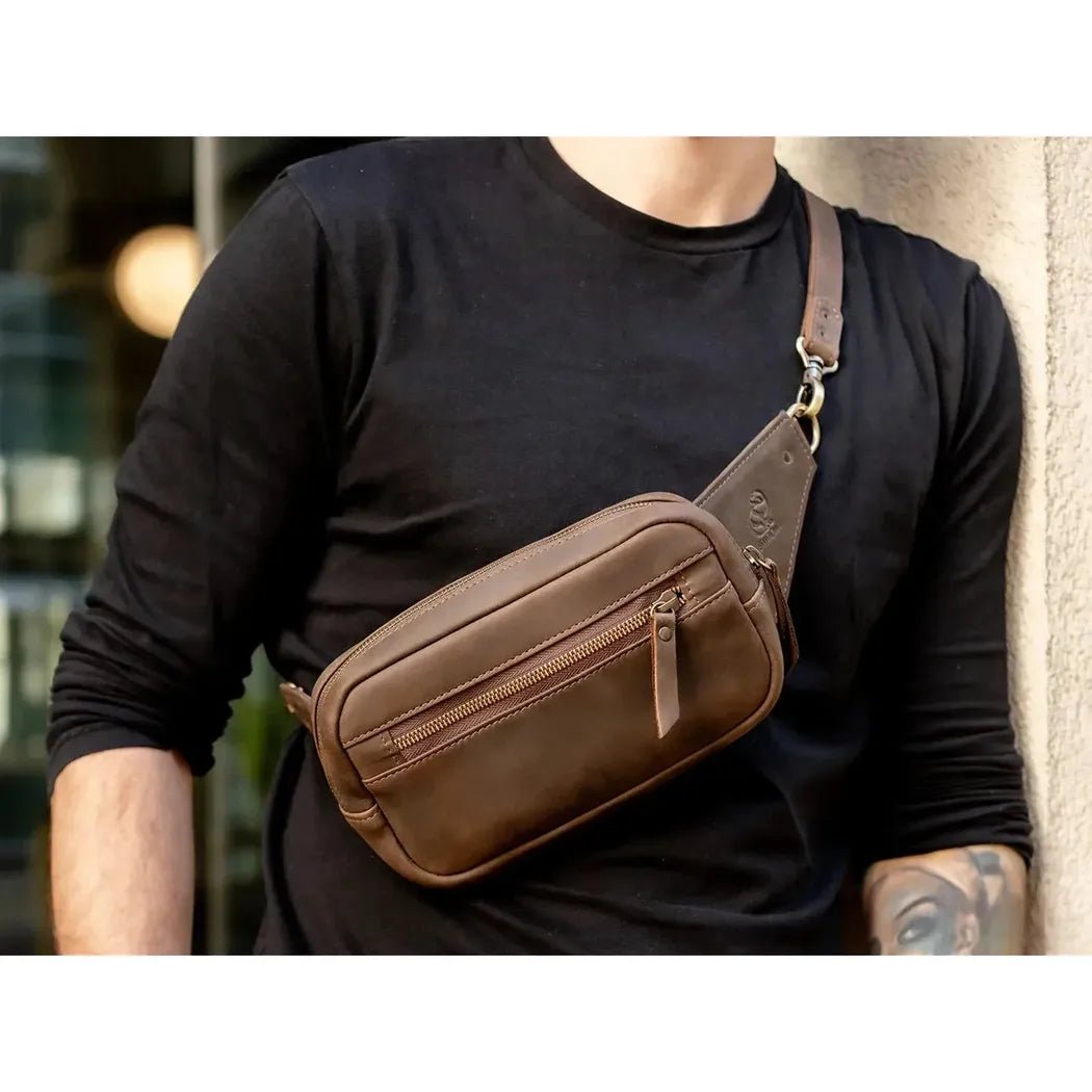 A man in a black shirt wears the brown Beavercraft Quest leather waist bag with a visible zipper and shoulder strap against a light wall.