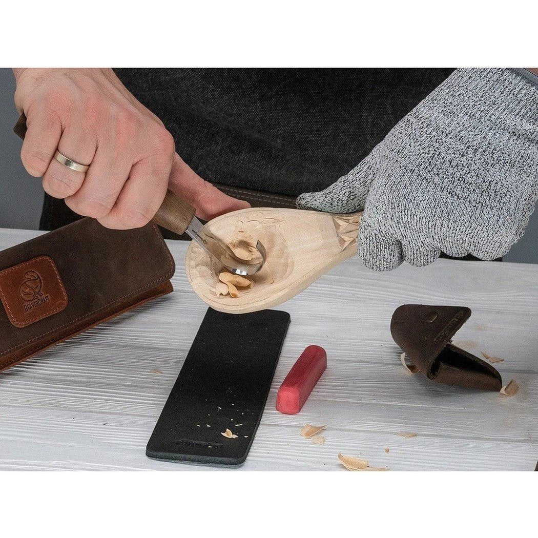 A person carves a wooden spoon with the Beavercraft Spoon Carving Tool Set in a genuine leather case on a light wood table.