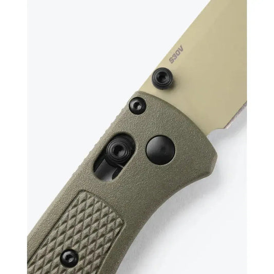 A close-up of the Benchmade Bugout knife with its olive handle and S30V blade, showing the textured grip and pocket clip against a white background.