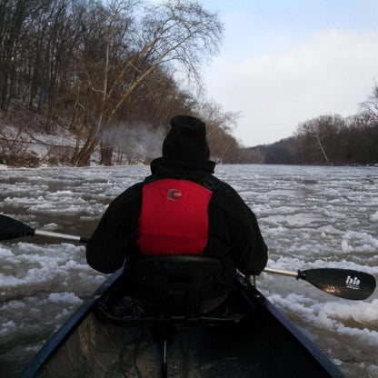 A person in a red life vest paddles a canoe on a partially frozen river with a black Bending Branches Whisper AS paddle.