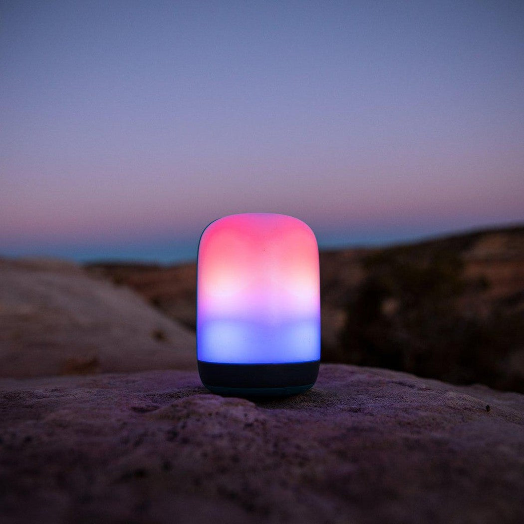 A BioLite Alpenglow 500 Lantern sits on a rock at dusk with a colorful gradient glow.