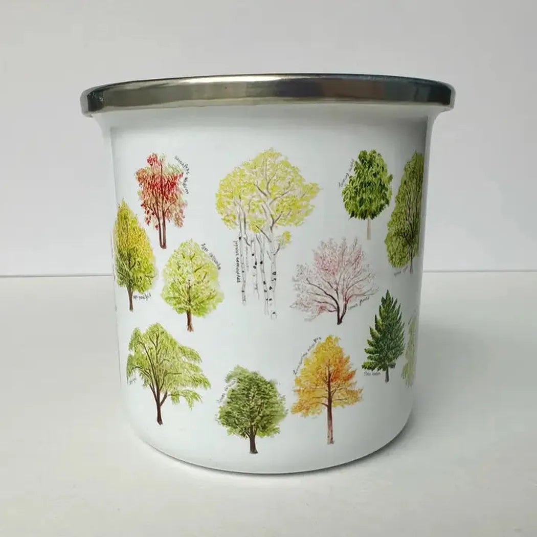 A white Brush & Bark Camping Mug with colorful tree illustrations on it sits on a white surface against a white background.