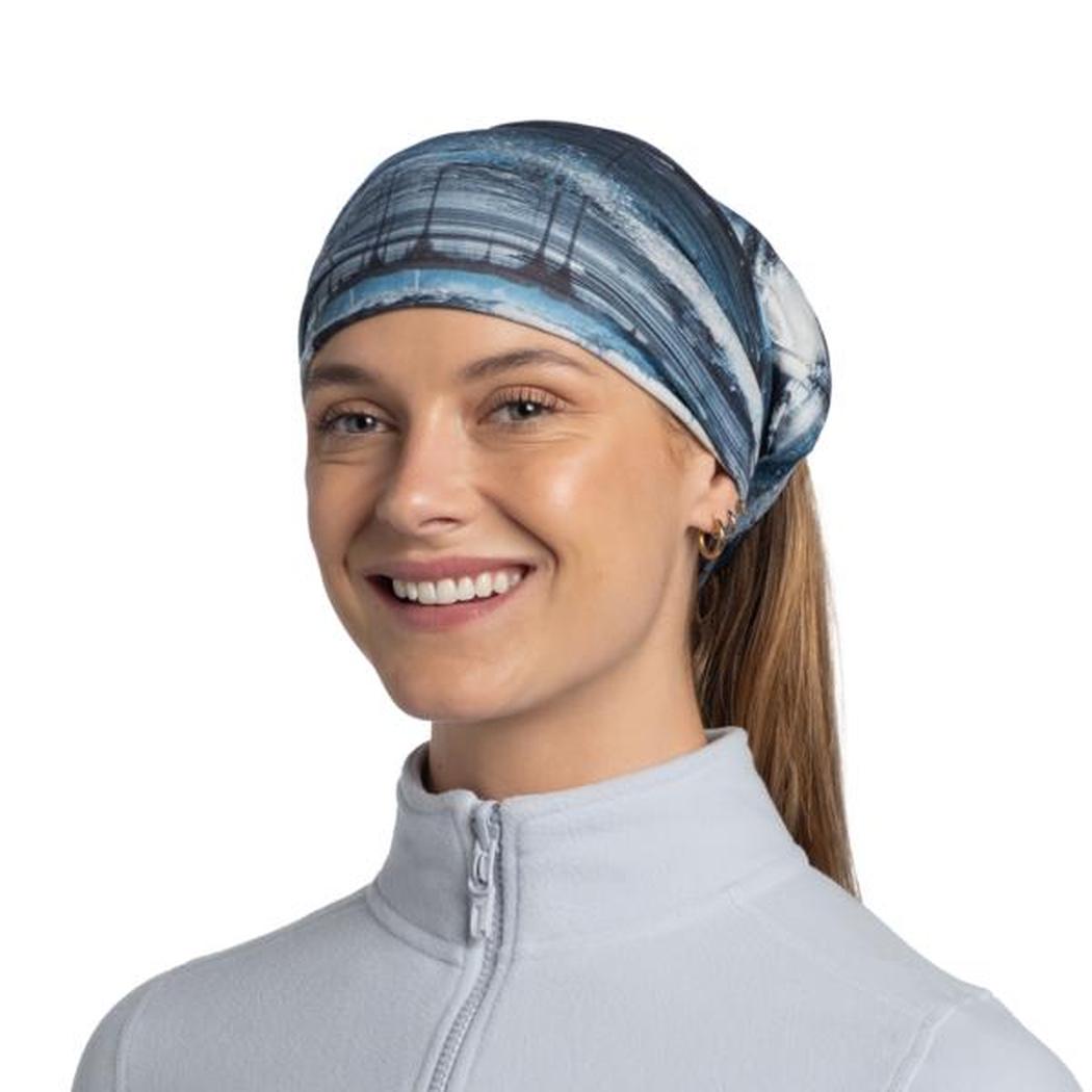 A woman wears the Blue Buff Original EcoStretch - Oser headband with a ponytail, against a plain white background.