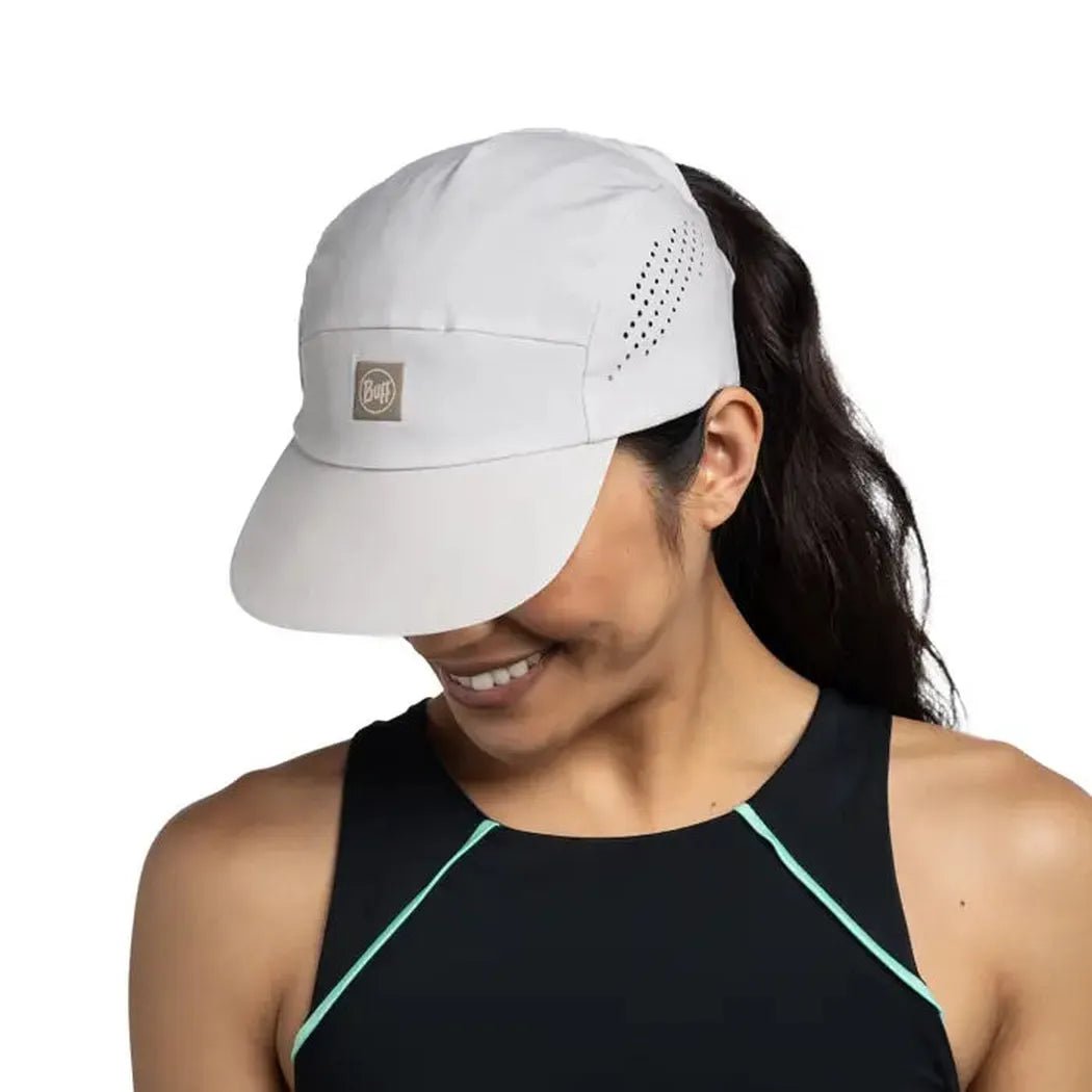 A woman wears the Birch Grey Buff Pack Speed Cap - Acro with a ponytail, against a white background.