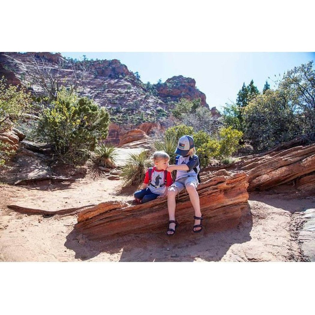 Two kids sit on a rock in a desert landscape wearing CamelBak Big Bite Valve hydration gear.