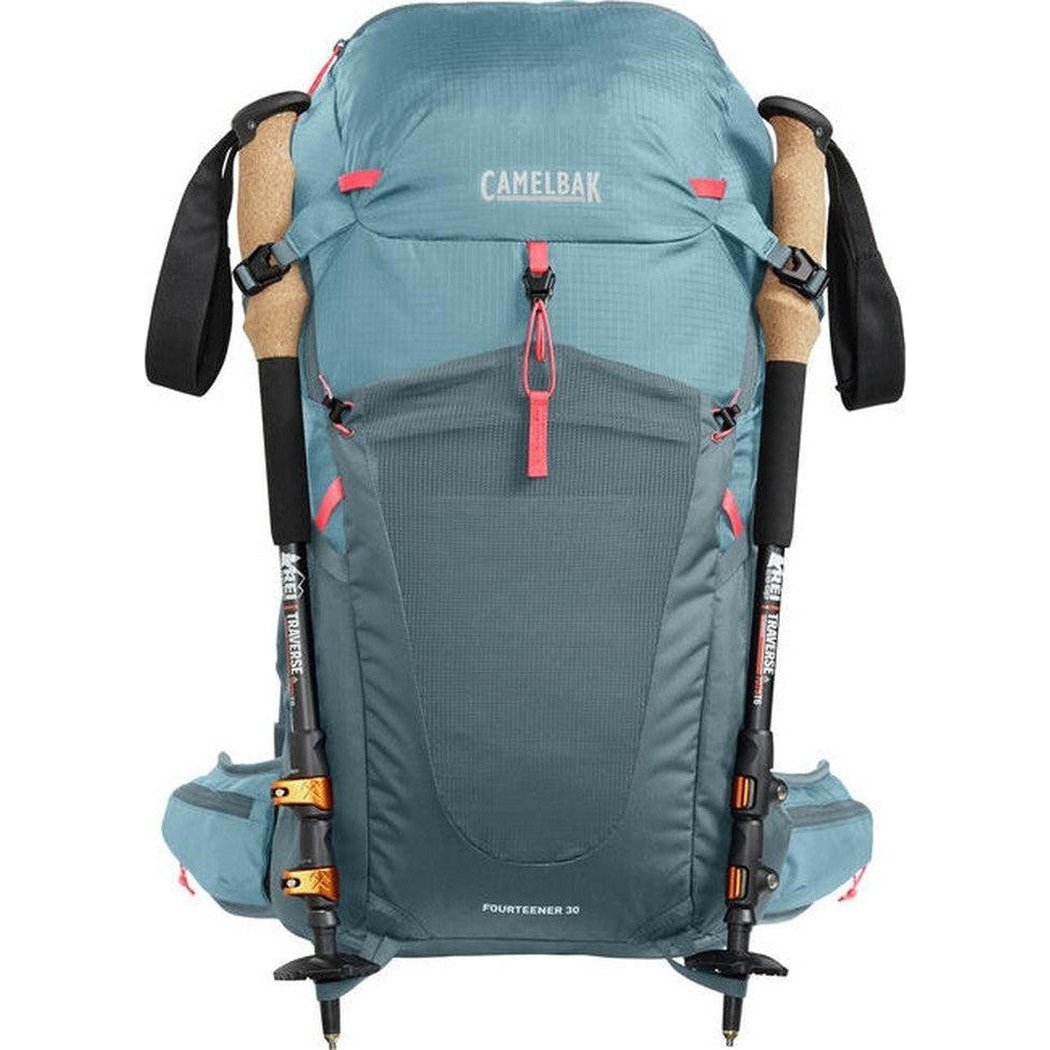 Back view of the CamelBak Women's Fourteener 30 in Smoke Blue/Fiery Coral with trekking poles attached.