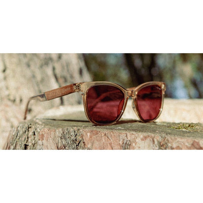 Side view of the Camp Eyewear Cove - Smokey Bear sunglasses with Desert frames and red lenses resting on a tree stump outdoors.