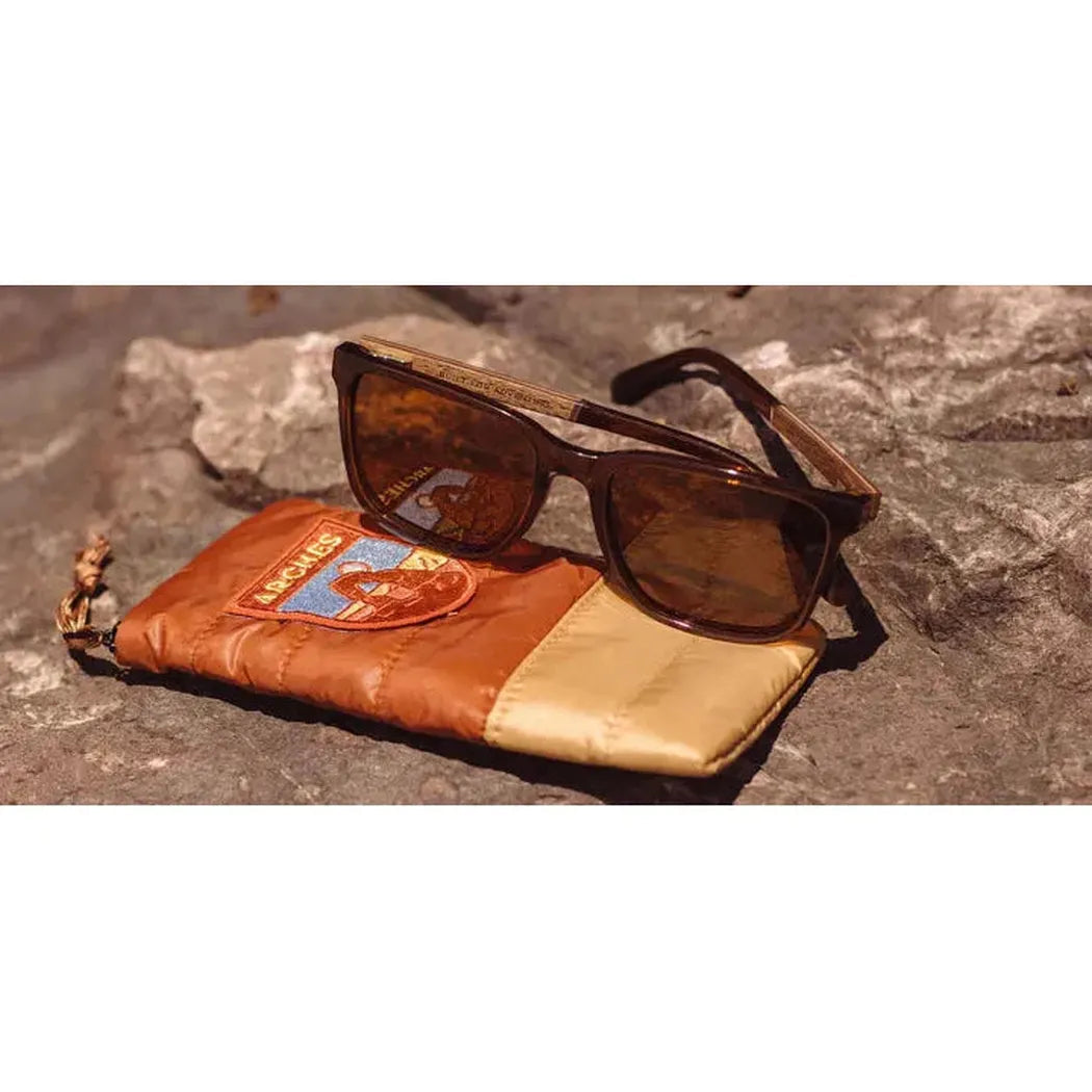 A pair of Camp Eyewear Crag - Arches Edition sunglasses rest on a brown and tan pouch with a logo, placed on a rocky surface.