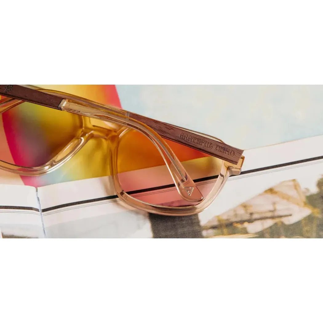 A pair of Camp Eyewear Glacier: Grateful Dead Bears Edition sunglasses with Desert // Grateful Dead Bears Engraved frames rests on an open magazine with colorful pages.