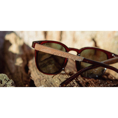 A close-up of the Camp Eyewear Topo - Smokey Bear sunglasses in Clay resting on a piece of wood with a blurred natural background.