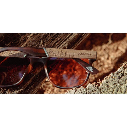 Side view of the Camp Eyewear Trail - Smokey Bear sunglasses with matte tortoise frames and brown lenses resting on a log.