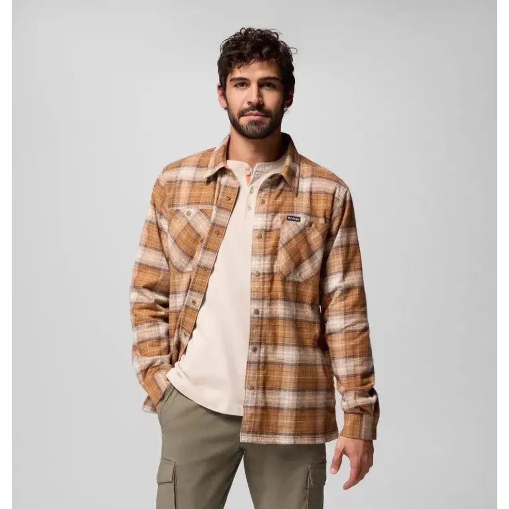 A model wearing the Columbia Sportswear Men's Cornell Woods Fleece Lined Shirt Jacket in Delta Lumberjack Tartan stands against a light gray background.