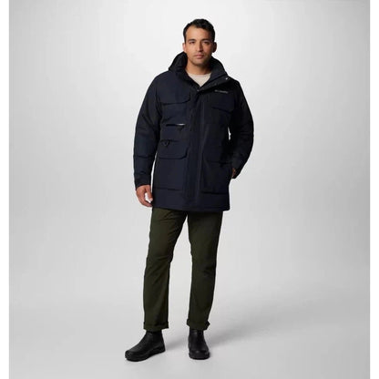 A front view of the Columbia Sportswear Men's Landroamer II Parka in Black on a model wearing olive pants and black boots against a light gray background.