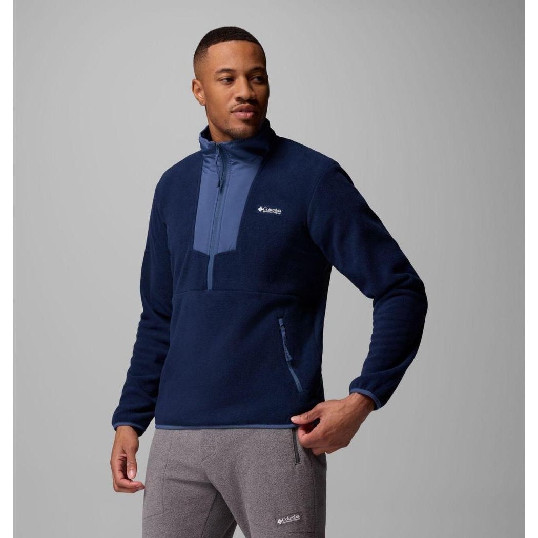 A man wearing the Columbia Sportswear Men's Sequoia Grove Half Zip Fleece in Collegiate Navy/Dark Mountain stands against a gray background.