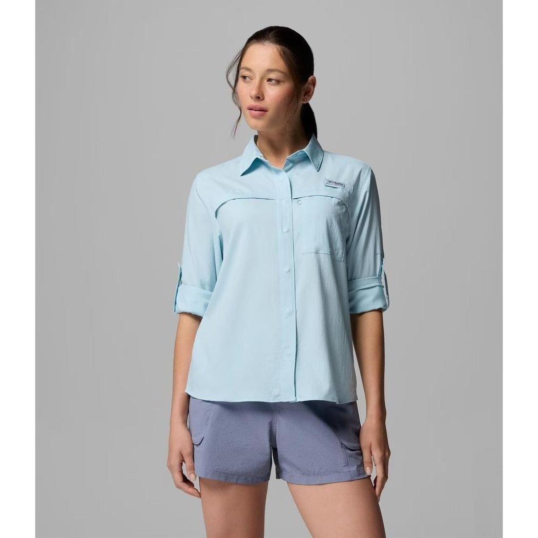 A woman wears the Columbia Sportswear Women's PFG Castback Woven Long Sleeve in Marine Light, with rolled sleeves, against a plain gray background.