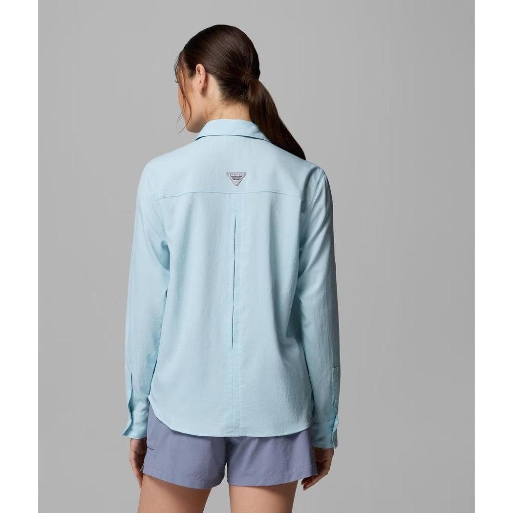 Back view of the Columbia Sportswear Women's PFG Castback Woven Long Sleeve in Marine Light on a model wearing light blue shorts against a gray background.
