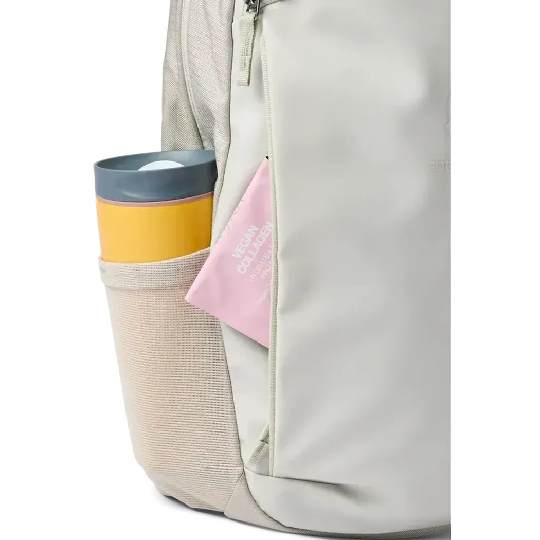 Side pocket of the Cotopaxi Allpa 18L Daypack in Mineral showing a yellow and gray tumbler and a pink item against a white background.